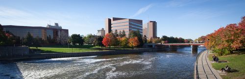 The image is of the University of Michigan building in Flint. There is a view of the building along a bridge and a river.